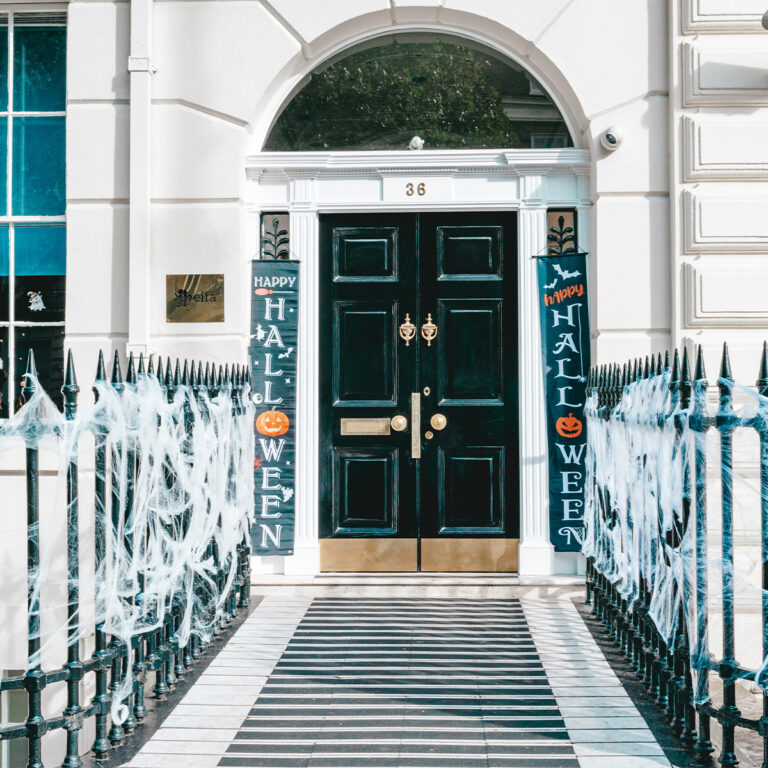 EIFA A white house entrance in London is beautifully decorated for Halloween. Black double doors with Happy Halloween signs on either side feature pumpkins and bats. White cobwebs drape the black iron gate, creating a bilingual welcome for trick-or-treaters.