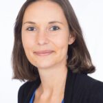 EIFA A bilingual woman with shoulder-length brown hair, wearing a blue top and black blazer, smiles gently against a plain white background.