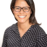 EIFA A smiling, bilingual person with shoulder-length hair and glasses, wearing a polka-dot patterned shirt, stands against a plain white background, reminiscent of a school portrait in cosmopolitan London.