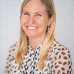 EIFA A smiling woman with long blonde hair and a patterned blouse stands against a light background, exuding the charm of a bilingual educator in London.
