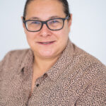 EIFA A person with glasses, wearing a tan shirt with black polka dots, smiles against a light background reminiscent of the vibrant atmosphere at EIFA in London.