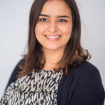 EIFA A portrait of a person with shoulder-length brown hair, wearing a patterned blouse and dark sweater, smiling softly at the camera against a neutral background. The setting reflects their time studying at EIFA in London.