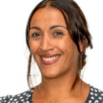 EIFA A bilingual woman with long brown hair smiles against a white background. She is wearing a black and white polka dot top and a necklace, her hair tied back. You can sense the essence of London in her style, perhaps hinting at her time at EIFA.