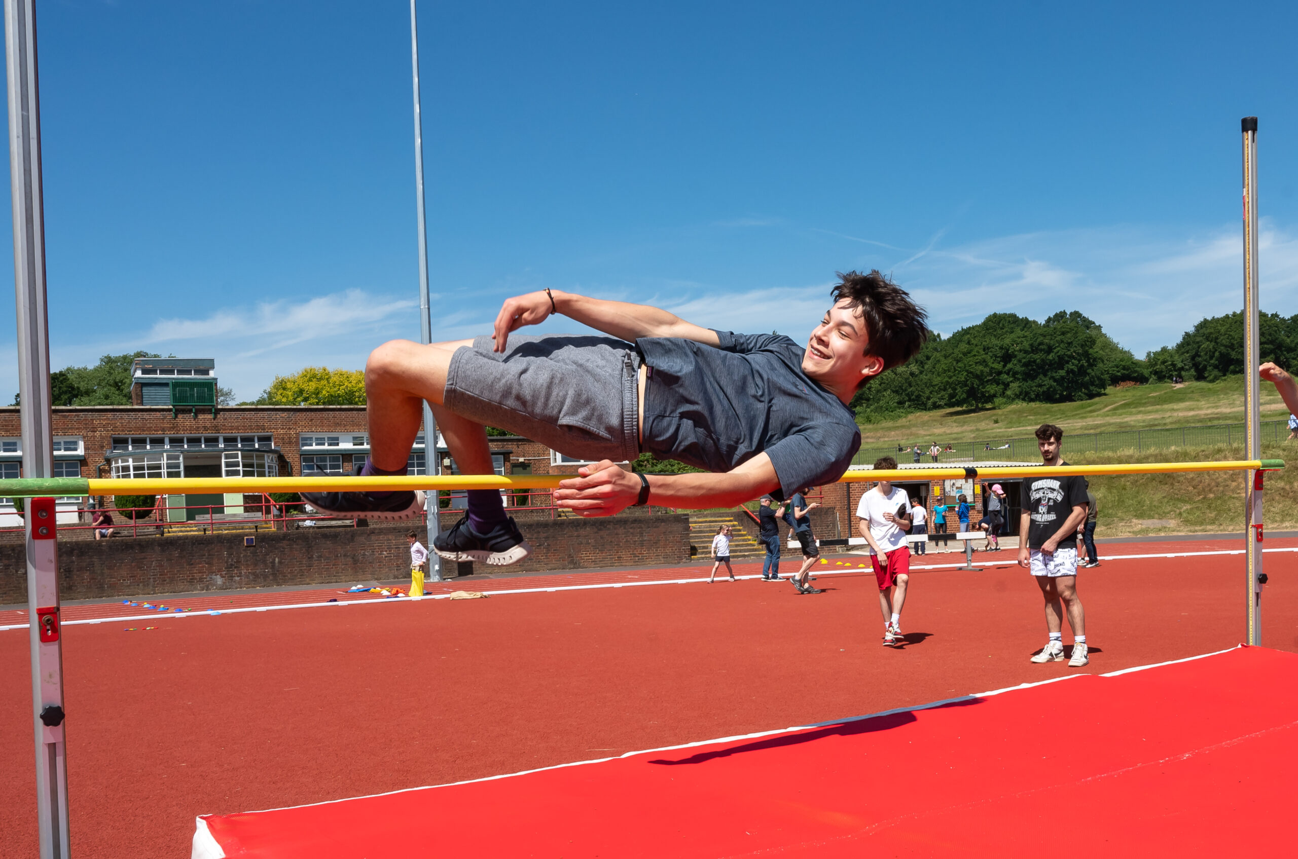 EIFA At a sunny track and field event in London, a young man in a gray t-shirt and shorts clears the high jump bar. Participants and spectators animate the background, echoing the vibrant spirit of EIFAs bilingual community.