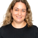 EIFA A bilingual woman with curly light brown hair, wearing a black long-sleeve top, smiles warmly against a white backdrop.