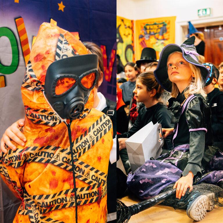 EIFA At a lively costume event in London, a person donned in a caution-tape wrapped hazmat suit with a gas mask stands next to a child from EIFA School, charmingly dressed as a witch in purple and black. The background buzzes with festive decorations and other costumed attendees.