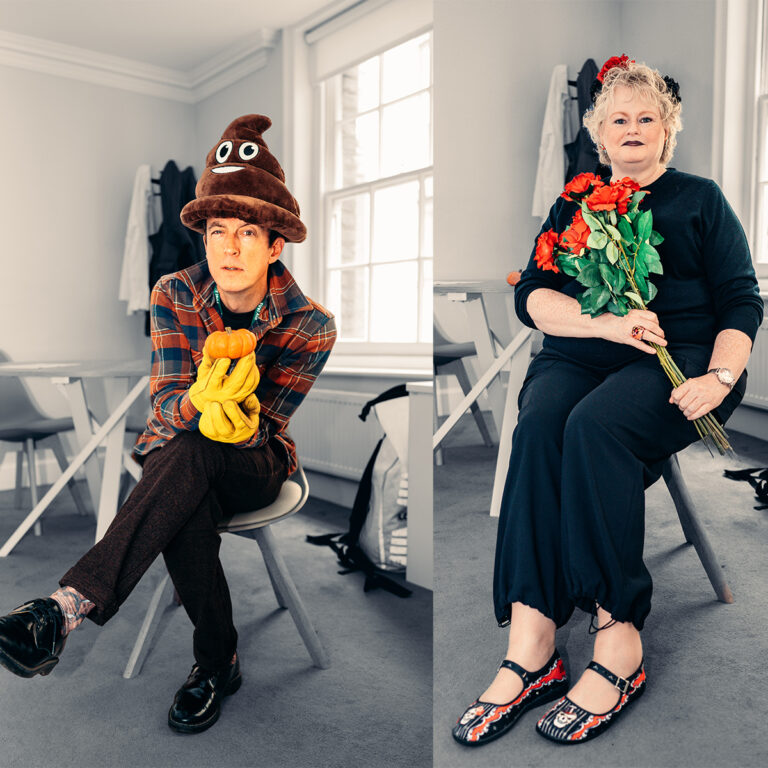 EIFA In a bright room with large windows, two people sit on chairs. The person on the left, wearing a brown hat resembling a poop emoji and yellow gloves, holds oranges. On the right, dressed in black and holding red flowers, sits someone from EIFA Bilingual School, smiling warmly.