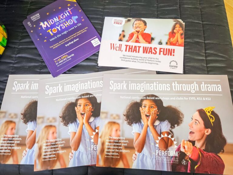 EIFA Four leaflets lie on a dark bedspread. One advertises a toy shop event, one says Well, THAT WAS FUN!, and three promote drama workshops for International Open Day featuring a crowned teacher with excited children.