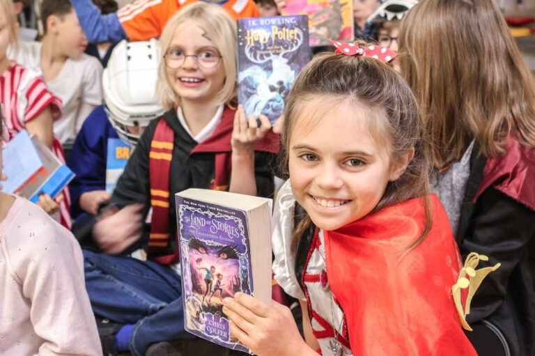 EIFA A smiling girl in a red cape holds a Land of Stories book, surrounded by other children in costumes at an International Open Day. One child dressed as Harry Potter holds a Harry Potter book, highlighting the event’s fun, book-themed atmosphere.