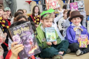EIFA A group of children in costumes hold up books while sitting on the floor at International Open Day. Some are dressed as book characters like Harry Potter and Willy Wonka, with smiles and excitement on their faces. EIFA A group of children in costumes hold up books while sitting on the floor at International Open Day. Some are dressed as book characters like Harry Potter and Willy Wonka, with smiles and excitement on their faces.