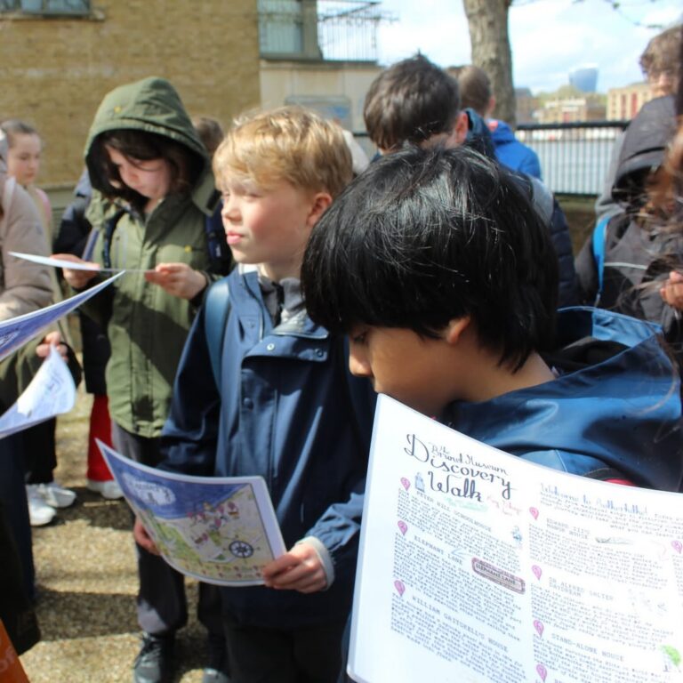 EIFA A group of children wearing jackets hold maps and information sheets while standing outside on a cloudy day, possibly participating in an educational discovery walk.
