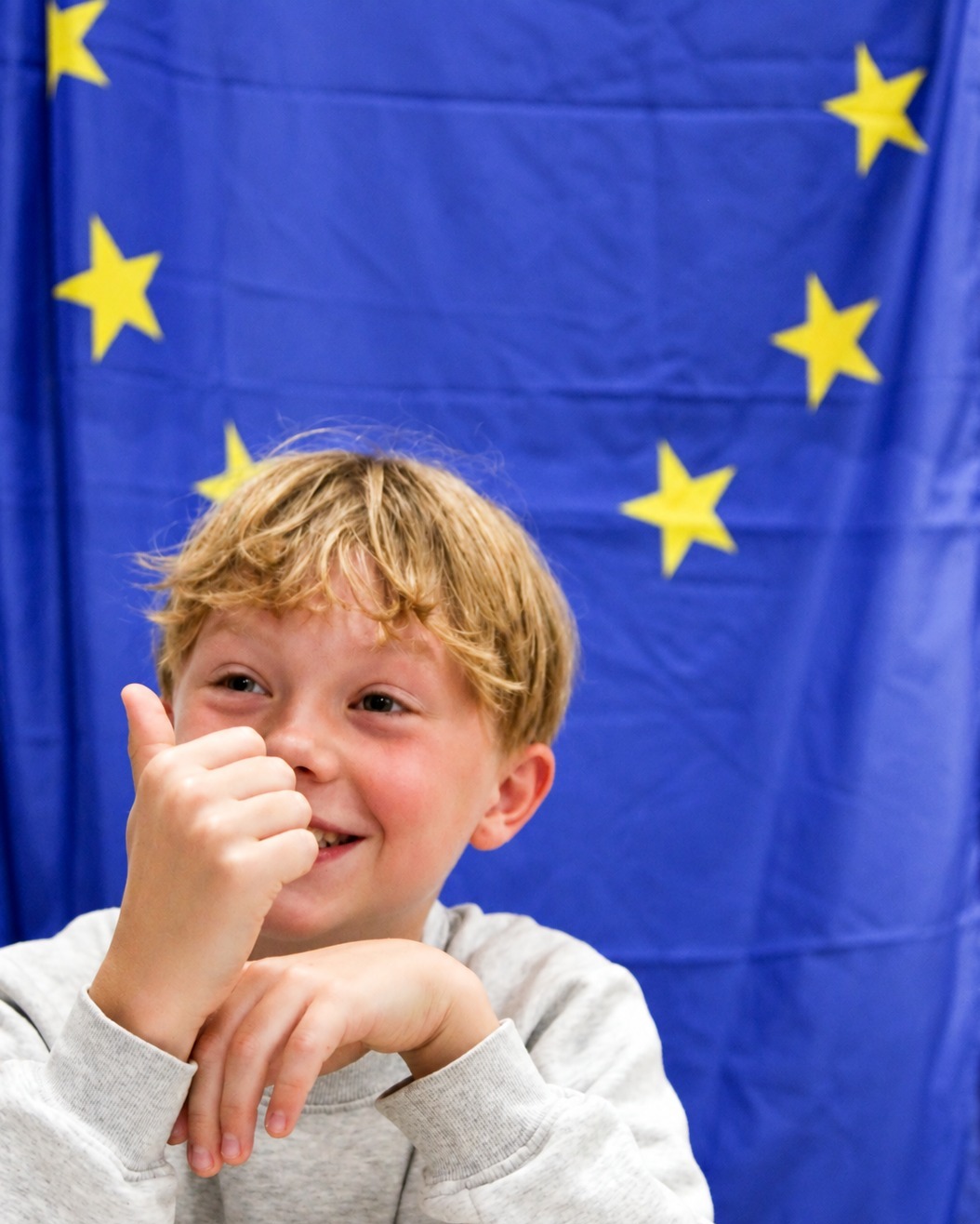 EIFA Un enfant souriant lève le pouce devant le drapeau de l'Union européenne.