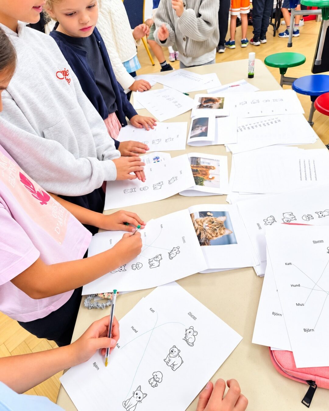 EIFA Un groupe d'enfants, assis à une table, remplit des fiches d'exercices sur le thème des animaux, comprenant des photos et des dessins d'animaux de compagnie.