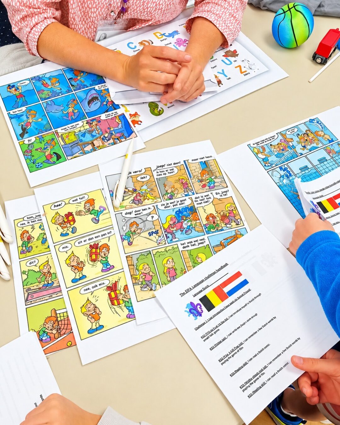 EIFA Des enfants assis à une table, en train de travailler sur des fiches d'apprentissage du néerlandais et des bandes dessinées.