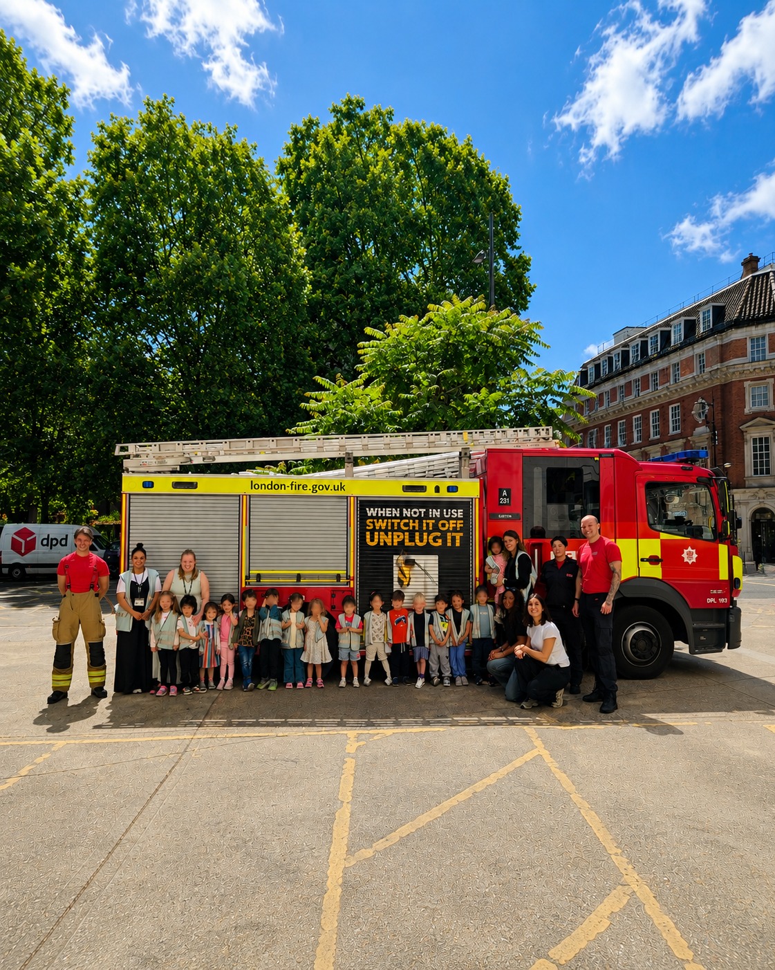 EIFA A group of children and adults stand in front of a London Fire Brigade fire truck with two firefighters, outside on a sunny day. The fire truck displays a safety message about unplugging devices.