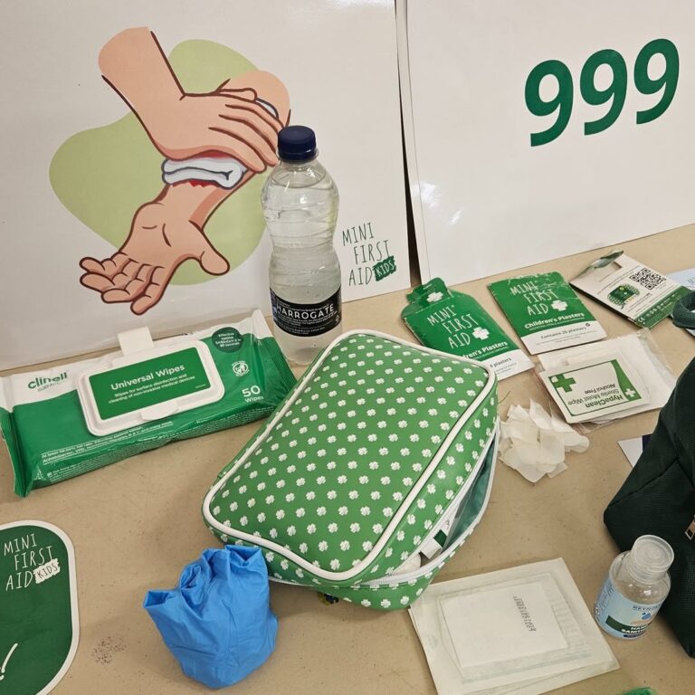 EIFA A green and white mini first aid kit with medical supplies, gloves, wipes, a water bottle, and a CPR instruction poster showing chest compressions. The emergency number 999 is visible in bold green text.
