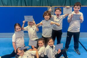 EIFA Huit enfants en tenue de sport posent sur le sol d’un gymnase, tenant des certificats et souriant fièrement. Derrière eux, un filet de volley-ball et un rideau bleu mettent en scène leur réussite, célébrée lors de la Journée mondiale de l’alimentation. EIFA Huit enfants en tenue de sport posent sur le sol d'un gymnase, tenant des certificats et souriant fièrement. Derrière eux, un filet de volley-ball et un rideau bleu mettent en scène leur réussite, célébrée lors de la Journée mondiale de l'alimentation.