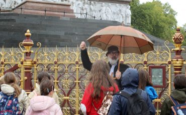 EIFA Un groupe d’enfants avec des sacs à dos écoute un homme tenant un parapluie devant une clôture ornée et un grand monument en pierre blanche, lors d’une Journée mondiale de l’alimentation nuageuse. EIFA Un groupe d'enfants avec des sacs à dos écoute un homme tenant un parapluie devant une clôture ornée et un grand monument en pierre blanche, lors d'une Journée mondiale de l'alimentation nuageuse.