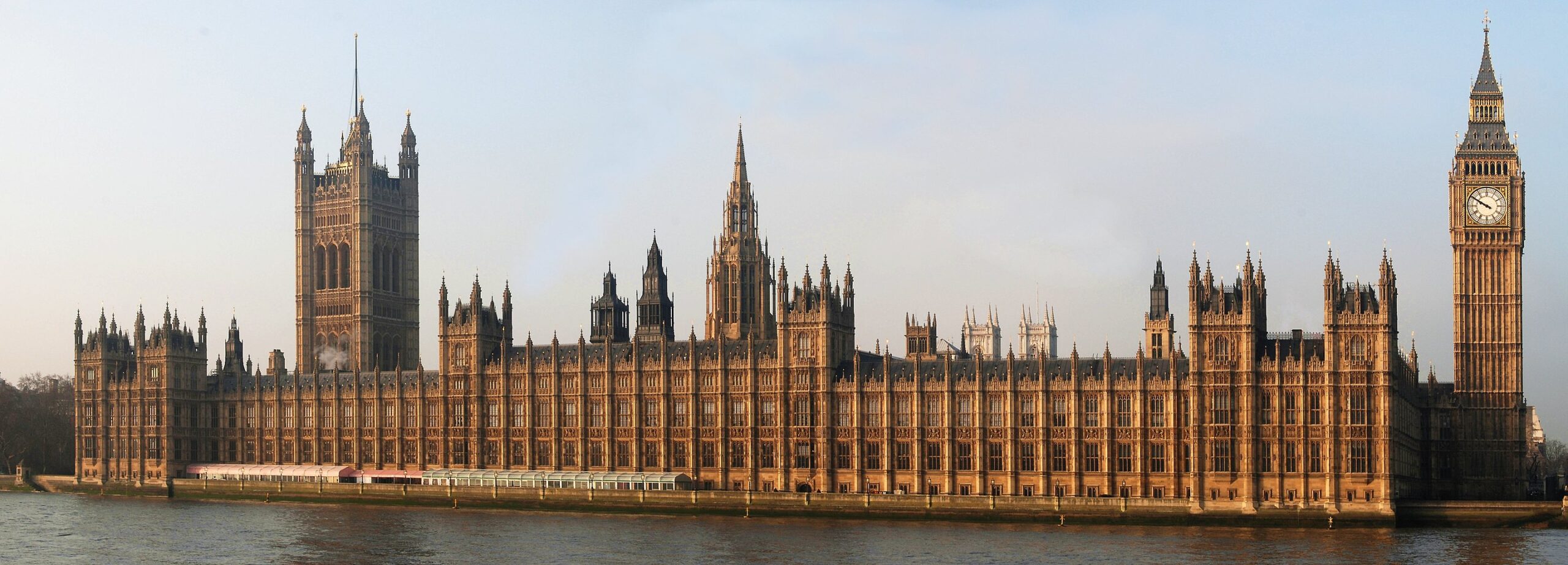 EIFA The image shows the Palace of Westminster, an iconic Gothic-style building in London, with the clock tower on the right known as Big Ben. Nearby, EIFA International School offers a bilingual curriculum. The structure is situated on the bank of the River Thames under a clear sky.