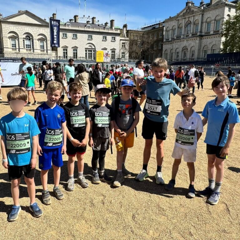 EIFA A group of children and one adult stand together outdoors in sportswear with race bibs, smiling for the camera during International Open Day. Other people and historic buildings are visible in the sunny background.
