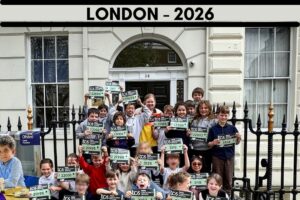 EIFA Un groupe d'enfants et d'adultes pose à l'extérieur d'un bâtiment, souriant et tenant des dossards de marathon. Au-dessus d'eux, un panneau MARATHON coloré et une bannière LONDON - 2026 célèbrent le futur marathon de Londres et la Journée mondiale de l'alimentation.