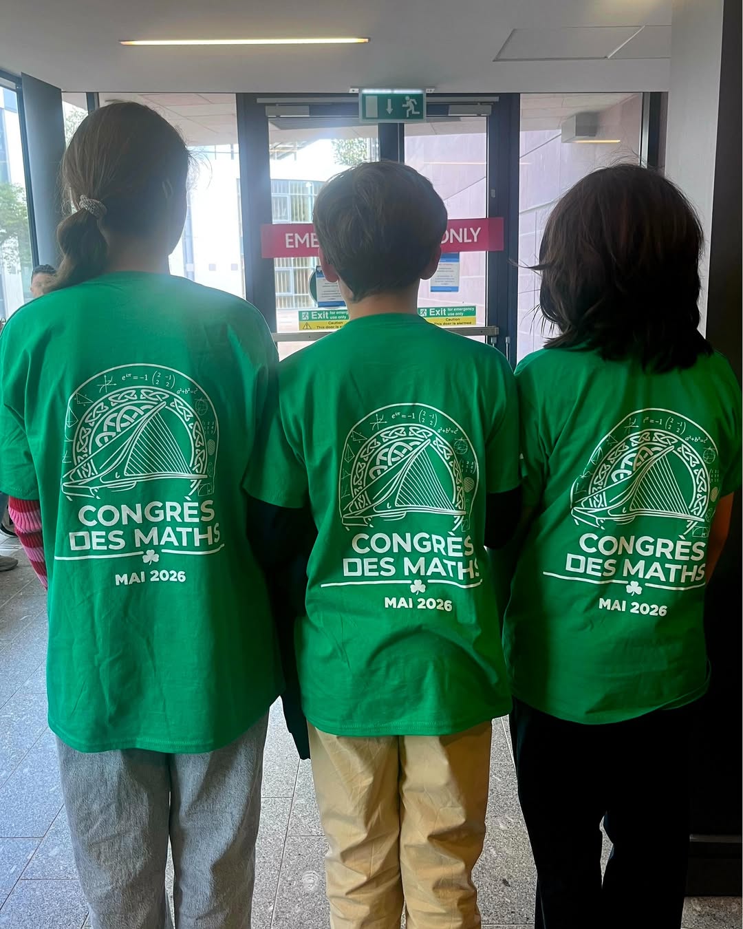 EIFA Three people stand indoors with their backs to the camera, wearing matching green shirts that read âCONGRĂS DES MATHS MAI 2026â with a mathematics-themed graphic above the text, celebrating International Open Day.