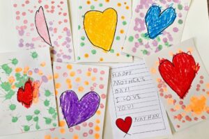 EIFA Sept cartes faites à la main et décorées de cœurs en crayon de couleur et de points peints sont disposées sur une table. L’une d’entre elles comporte un message écrit à la main : Bonne fête des mères ! Je t’aime. Nathan avec un dessin de cœur rouge. EIFA Sept cartes faites à la main et décorées de cœurs en crayon de couleur et de points peints sont disposées sur une table. L'une d'entre elles comporte un message écrit à la main : Bonne fête des mères ! Je t'aime. Nathan avec un dessin de cœur rouge.