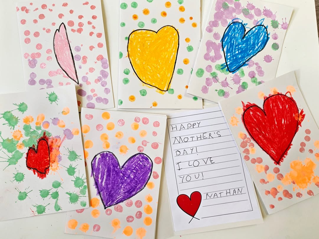 EIFA Seven handmade cards are displayed, each featuring colorful hearts and decorative dots or paint splatters. One card has a handwritten message: Happy Mothers Day! I love you signed by Nathan, with a small red heart drawing.