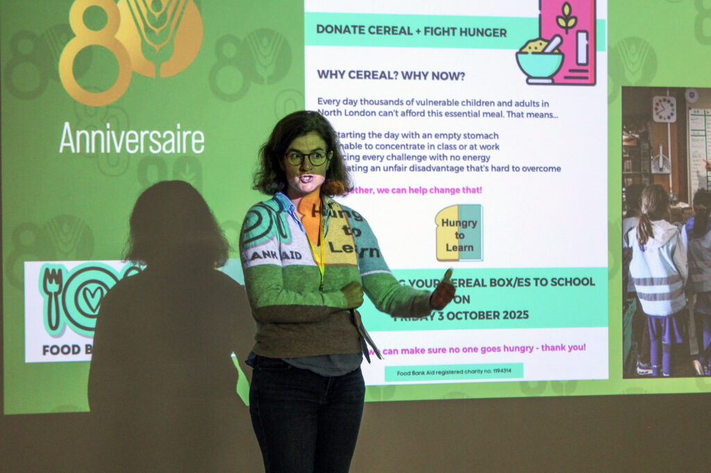 EIFA A woman stands in front of a projected presentation about donating cereal to fight hunger, with colorful graphics and text in both English and French displayed on the screen behind her.