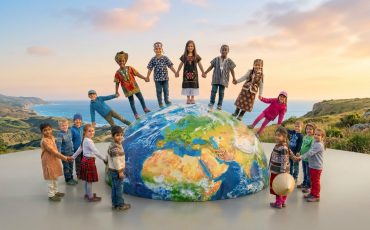 EIFA Children from diverse backgrounds in colorful clothing stand holding hands around a large globe outdoors, celebrating International Open Day and symbolizing unity and global friendship beneath a bright sky.
