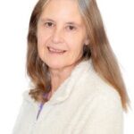 EIFA A woman with long, straight, light brown hair and gray streaks smiles gently. She is wearing a white, fuzzy zip-up jacket and is posed against a plain white background.