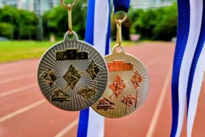EIFA Deux médailles, l'une d'or et l'autre d'argent, sont suspendues à des rubans bleus et blancs devant une piste de course en plein air. Marquant la première et la deuxième place, elles célèbrent la réussite - parfaites pour honorer les gagnants lors de la Journée mondiale de l'alimentation.