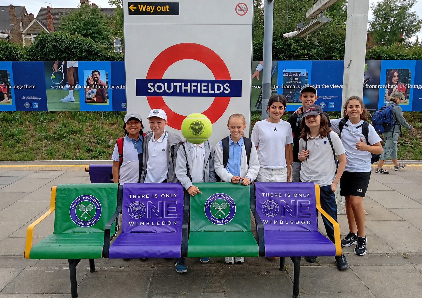 EIFA A group of kids in sportswear pose at Southfields Underground station with tennis props and Wimbledon banners on benches behind them, celebrating International Open Day.
