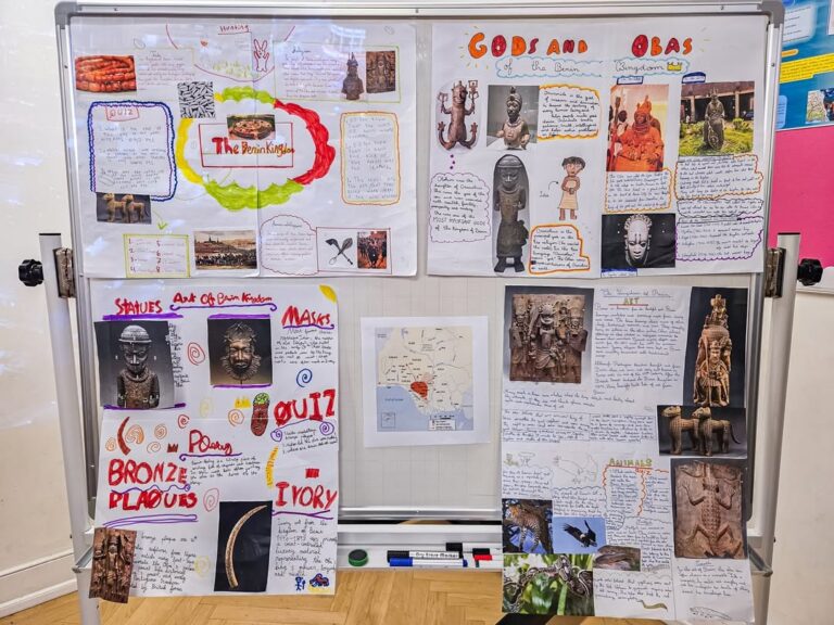 EIFA A classroom display board with colorful handwritten and illustrated posters about the Benin Kingdom, including information on gods, obas, bronze plaques, shrines, ivory, and maps, with photos of artifacts and quizzes.