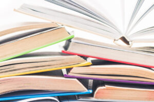 EIFA A vibrant stack of open books, reminiscent of a cozy Soho nook, is set in two rows with their pages artfully fanned out. The colorful covers, in shades like blue and green, invite readers to discover new stories against a plain white backdrop.