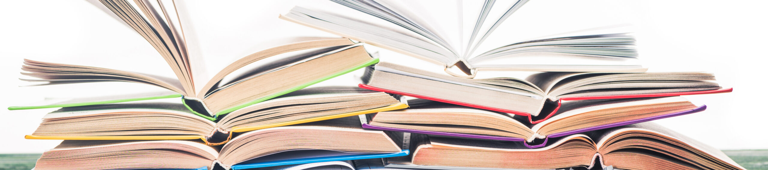EIFA A vibrant stack of open books, reminiscent of a cozy Soho nook, is set in two rows with their pages artfully fanned out. The colorful covers, in shades like blue and green, invite readers to discover new stories against a plain white backdrop.