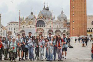 EIFA A group of people pose for a photo in St. Mark’s Square in Venice, Italy, with St. Mark’s Basilica and the Campanile behind them—just as Year 3 and Year 4 visited the Isle of Wight, they’re enjoying a lively plaza filled with tourists and historic buildings.