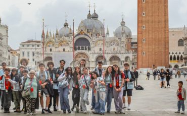 EIFA A group of people pose for a photo in St. Mark’s Square in Venice, Italy, with St. Mark’s Basilica and the Campanile behind them—just as Year 3 and Year 4 visited the Isle of Wight, they’re enjoying a lively plaza filled with tourists and historic buildings.