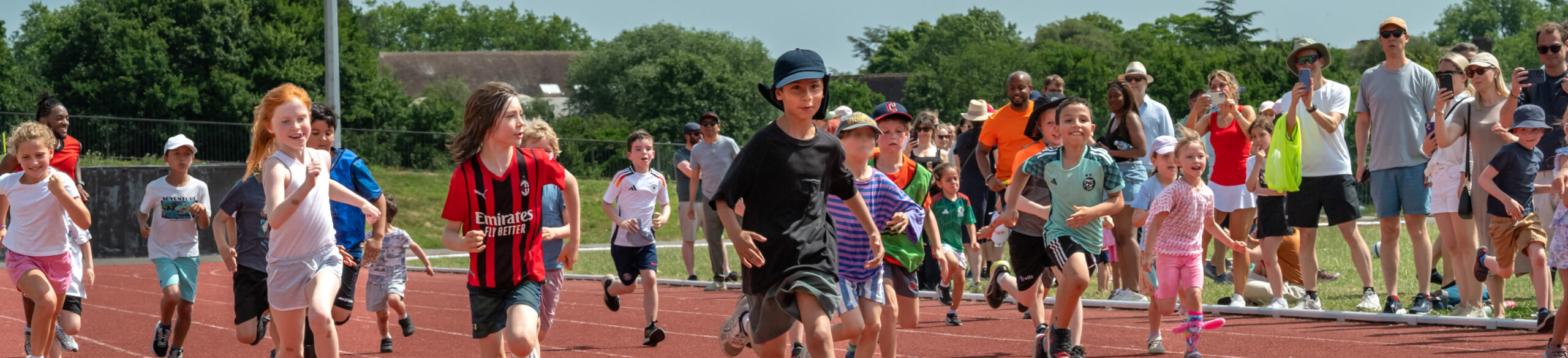 EIFA Un groupe d'enfants, inspiré par la classe de MS qui a visité le Hampton Court Palace, fait une course sur une piste en plein air tandis que des spectateurs regardent et encouragent depuis les lignes de touche par une journée ensoleillée.