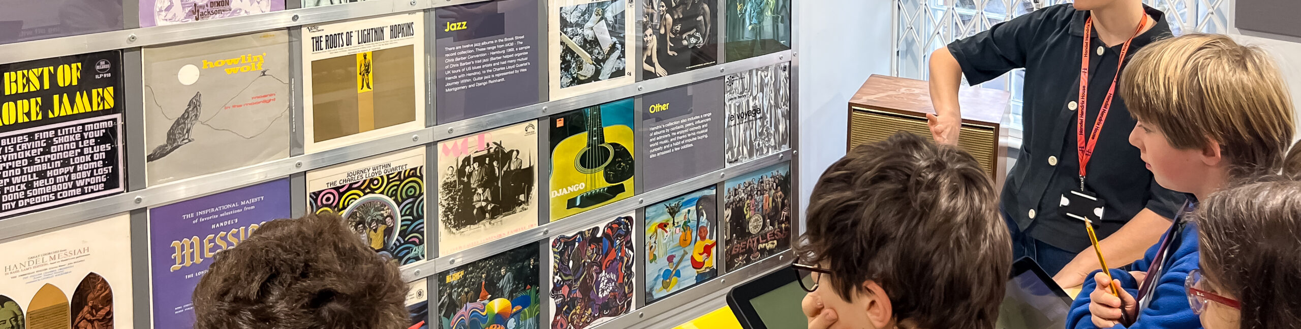 EIFA A group of people gathered around a vintage vinyl record display in London, including various album covers. One person stands, gesturing as if explaining something to the assembled EI students, while others are seated and looking on with interest.