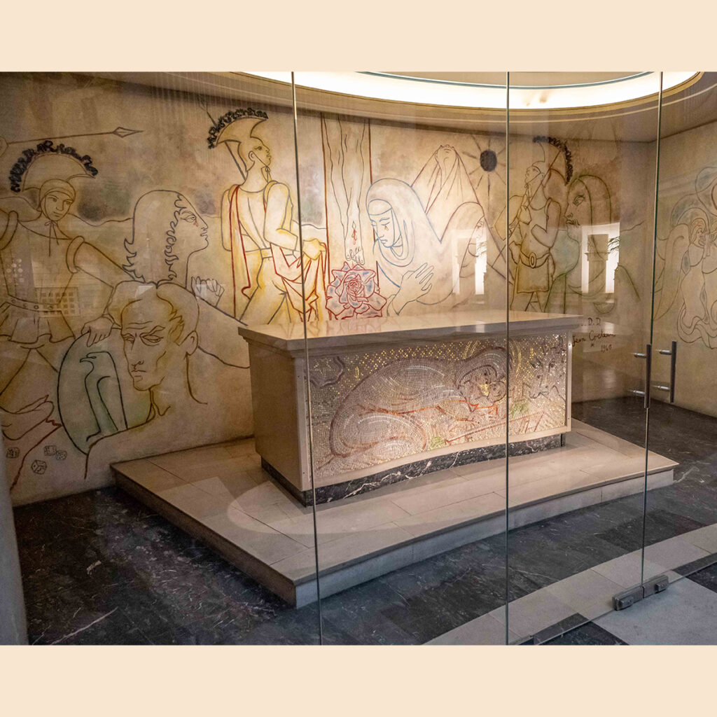 EIFA Une salle aux parois vitrées abrite un autel en pierre décoré dune sculpture détaillée. Les murs environnants sont ornés de dessins au trait représentant des personnages historiques ou mythiques engagés dans diverses activités. Le plafond est arrondi et doucement éclairé.