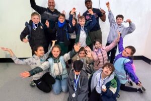 EIFA Un groupe d’enfants souriants portant des médailles posent avec enthousiasme avec deux adultes à l’intérieur, levant les bras et célébrant ensemble la Journée mondiale de l’alimentation. Certains enfants sont agenouillés devant, tandis que d’autres sont debout derrière eux. EIFA Un groupe d'enfants souriants portant des médailles posent avec enthousiasme avec deux adultes à l'intérieur, levant les bras et célébrant ensemble la Journée mondiale de l'alimentation. Certains enfants sont agenouillés devant, tandis que d'autres sont debout derrière eux.