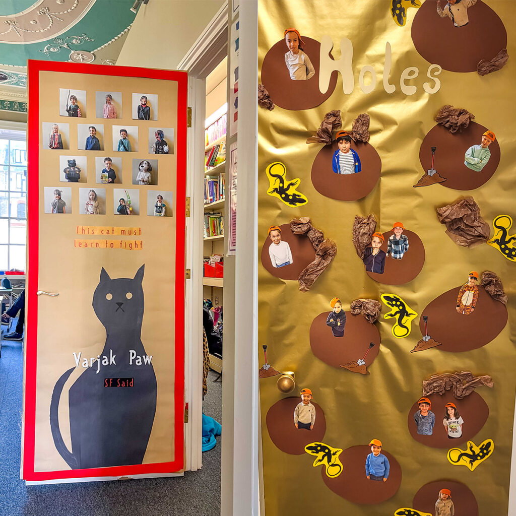 EIFA À gauche : Porte décorée d'une illustration de chat noir et d'images d'élèves portant des bonnets colorés, avec la légende « Yarjak Paw a dit que les apprenants internationaux se battent ». À droite : Porte sur le thème du livre « Holes », avec des images de personnages, des collines de papier et des lézards jaunes.